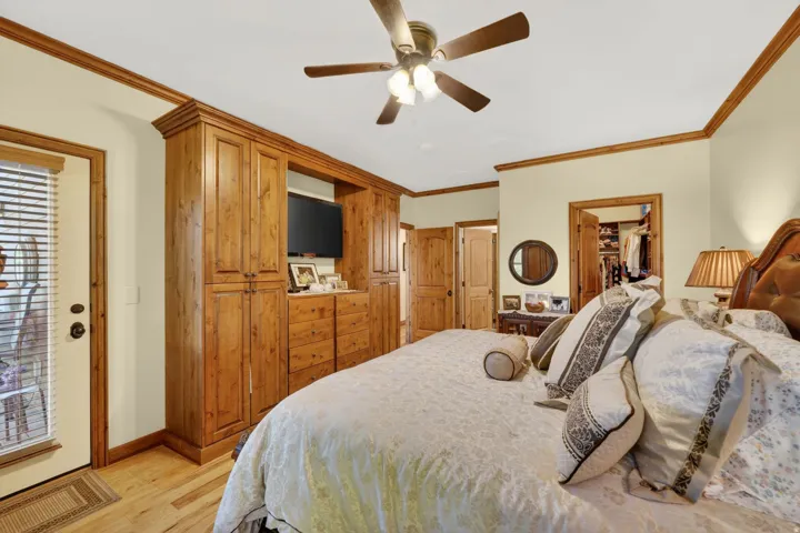 Expansive room featuring hardwood flooring, built-in cabinetry with integrated media storage, a ceiling fan with integrated lighting, and crown molding