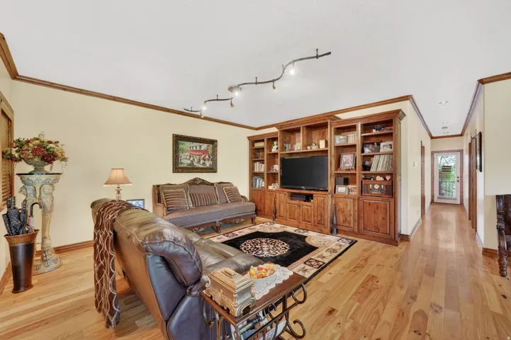 Spacious living area featuring extensive built-in wooden shelving, wood-finish flooring, recessed lighting, and crown molding