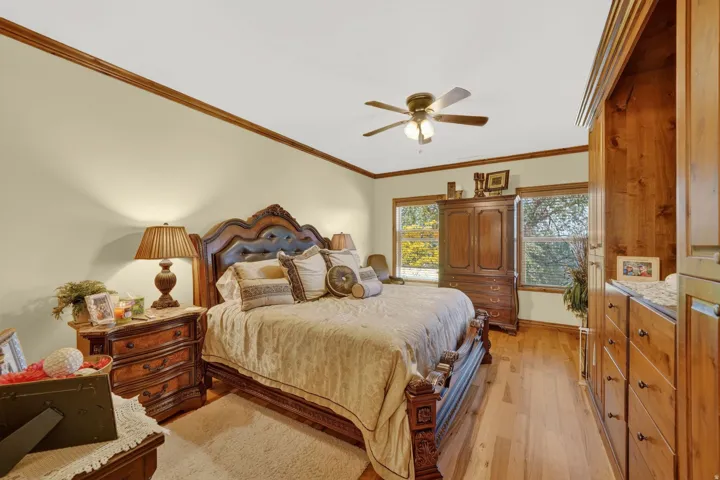 Bedroom featuring wood-finish flooring, a ceiling fan, crown molding, and two windows