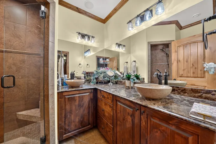 Glass-enclosed shower with a tiled bench and a dual-sink vanity featuring stone vessel sinks, dark wood cabinetry, and a polished stone countertop