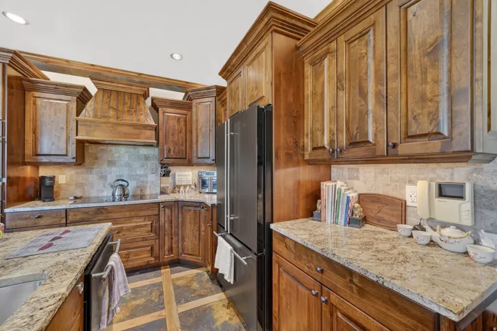 Kitchen featuring rich wood cabinetry, patterned tile backsplash, light-toned granite-style countertops, and integrated black appliances
