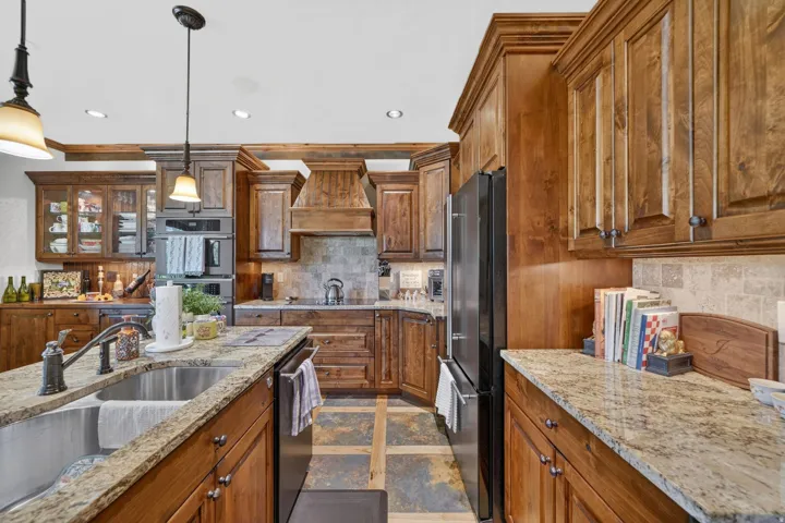 Kitchen featuring rich wood cabinetry, granite countertops, stainless steel undermount sink, built-in double oven, and tile flooring