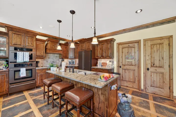 Spacious kitchen featuring custom wood cabinetry, a large kitchen island with a stone countertop, a built-in double oven, and pendant lighting