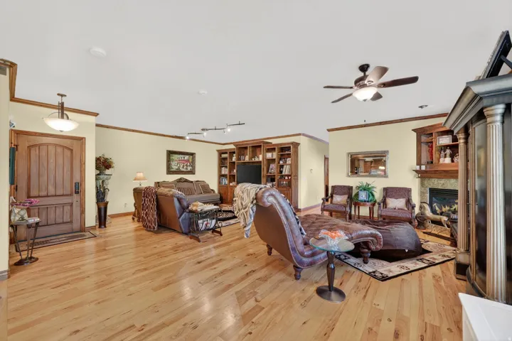 Expansive living area featuring light wood-finish flooring throughout, a ceiling fan with integrated lighting, and crown molding