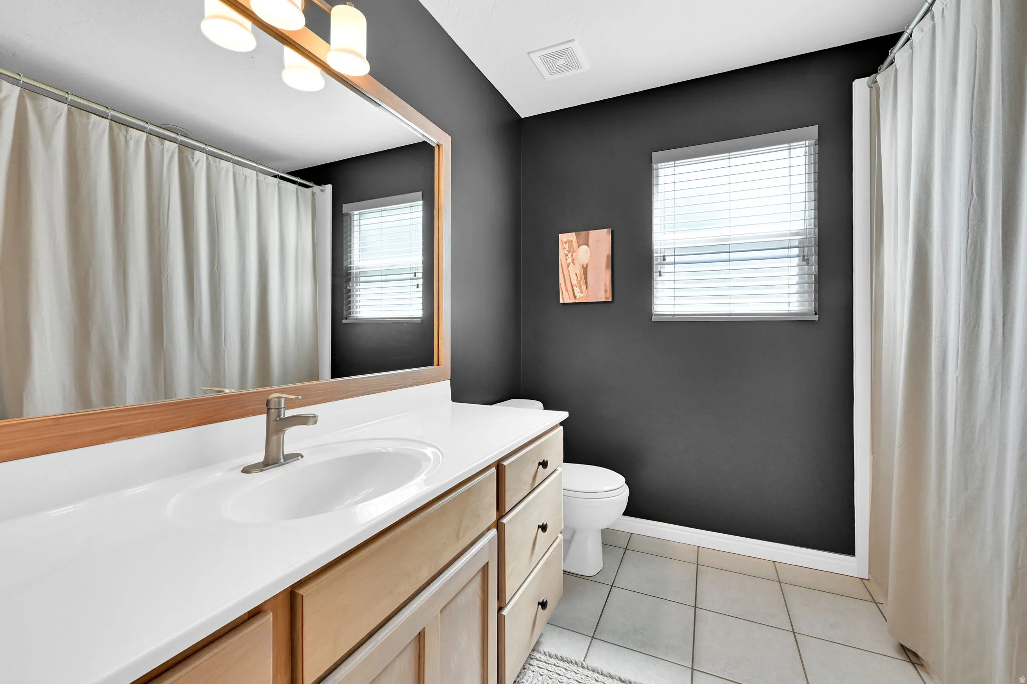 Bathroom featuring a wood-finish vanity with a white countertop and integrated sink, brushed nickel faucet, and tile flooring