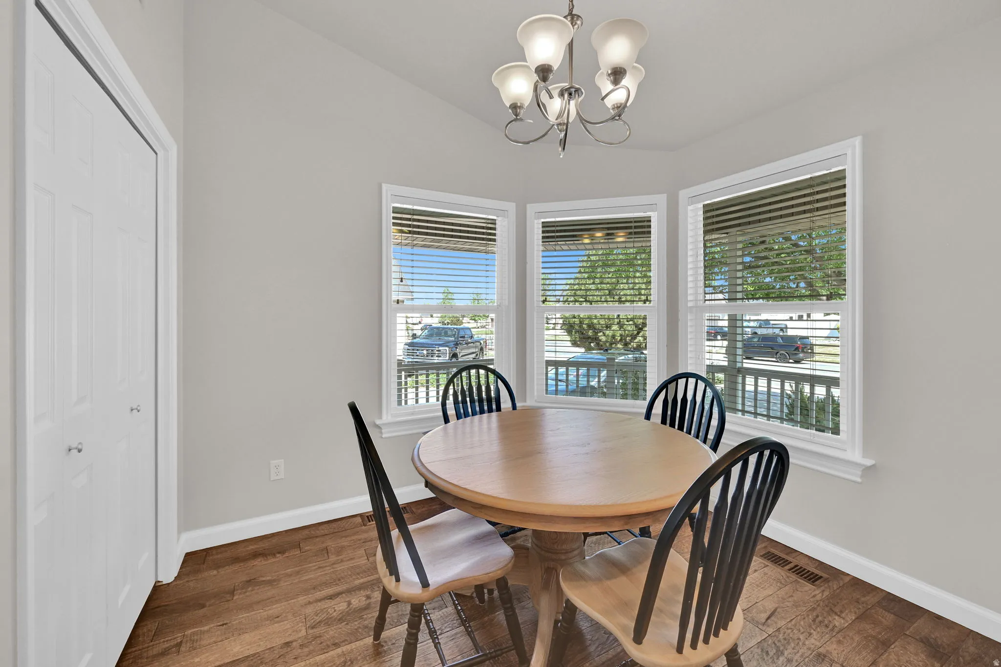 Dining area featuring a bay window, wood-finish flooring, a contemporary chandelier, and a white bi-fold closet