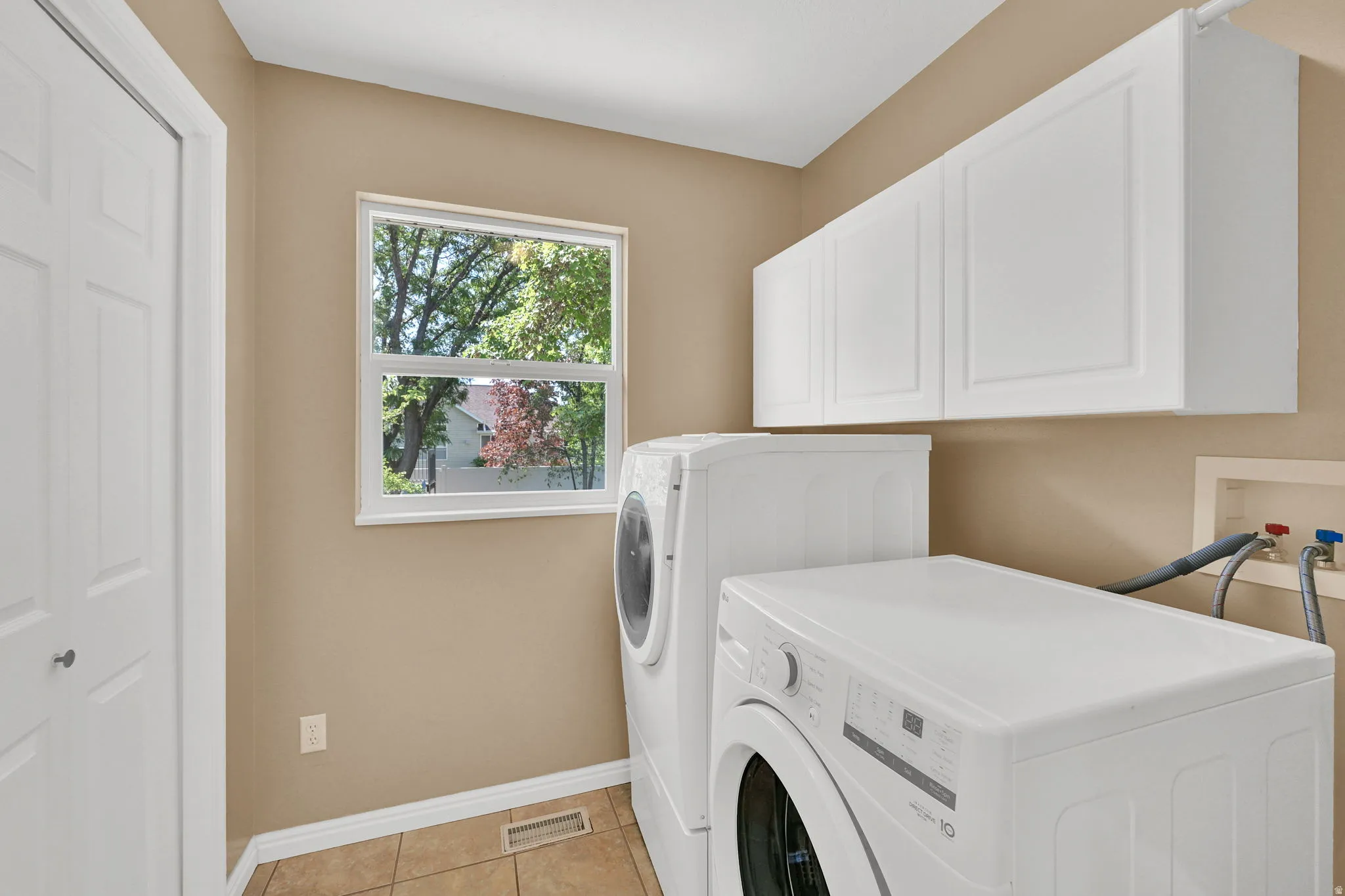 Laundry area featuring a window, white cabinetry, a bi-fold door, and tile flooring