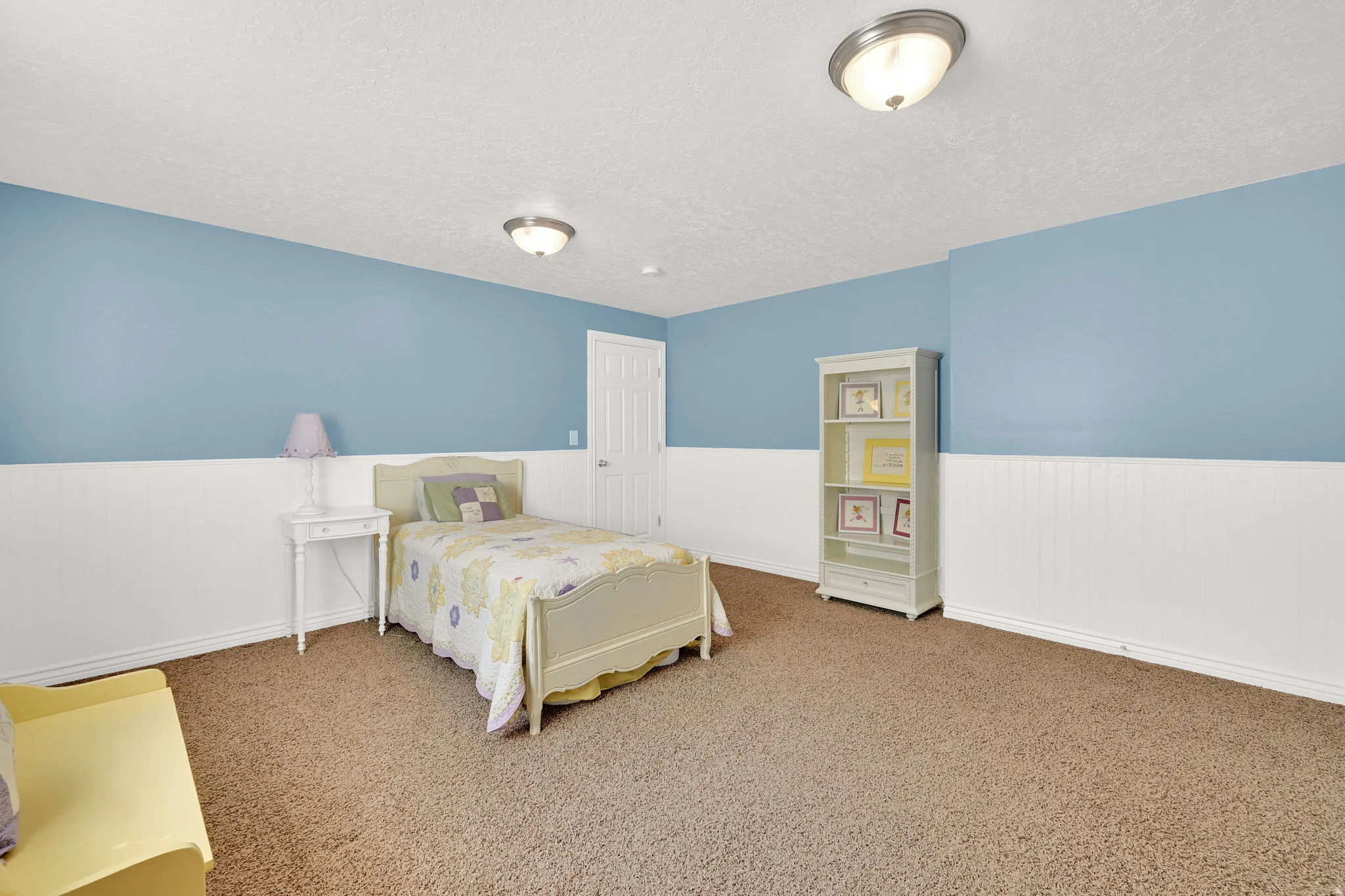 Spacious room featuring light blue walls with white wainscoting, brown carpet flooring, and white trim