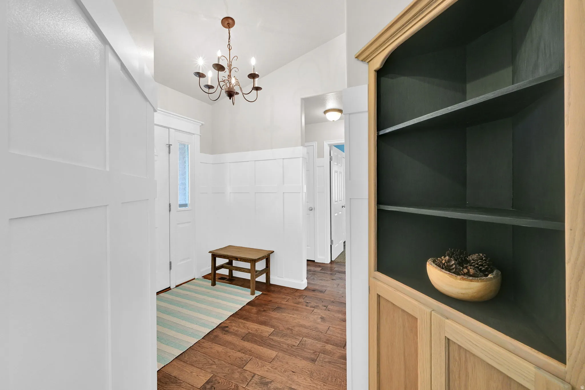 Entryway featuring wood-finish flooring, white wainscoting, and an overhead chandelier