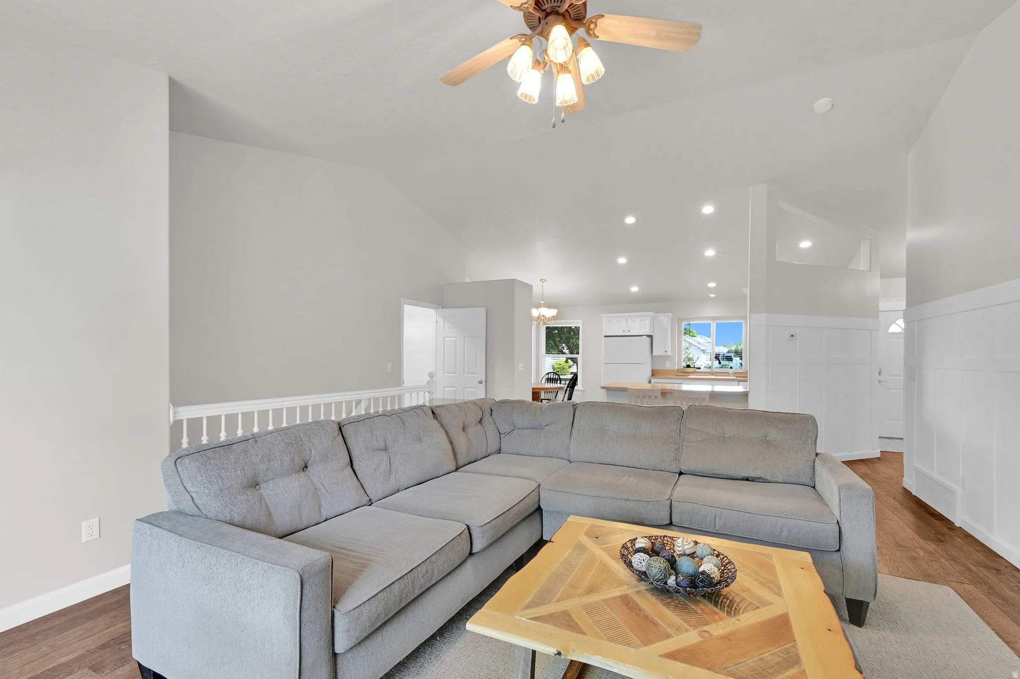 Spacious living room featuring vaulted ceilings, a ceiling fan, recessed lighting, wood-finish flooring, and white paneled walls