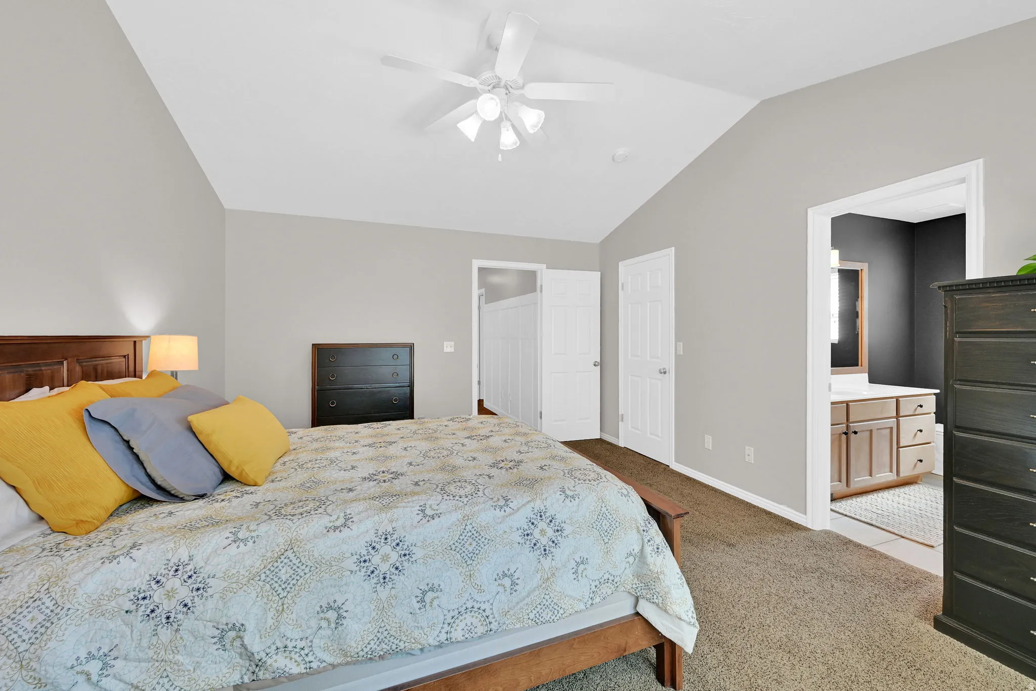 Carpeted bedroom featuring vaulted ceilings, light gray wall paint, and a ceiling fan