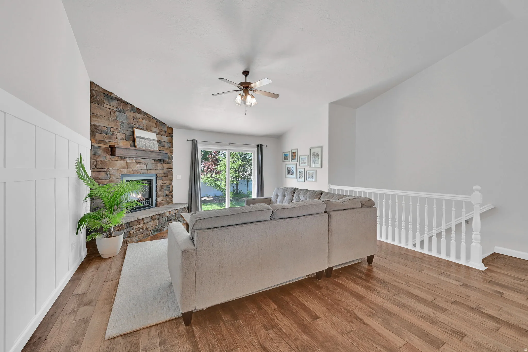 Living area featuring wood-finish flooring, a stone-clad fireplace with a dark wood mantel, board and batten accent wall, and vaulted ceilings