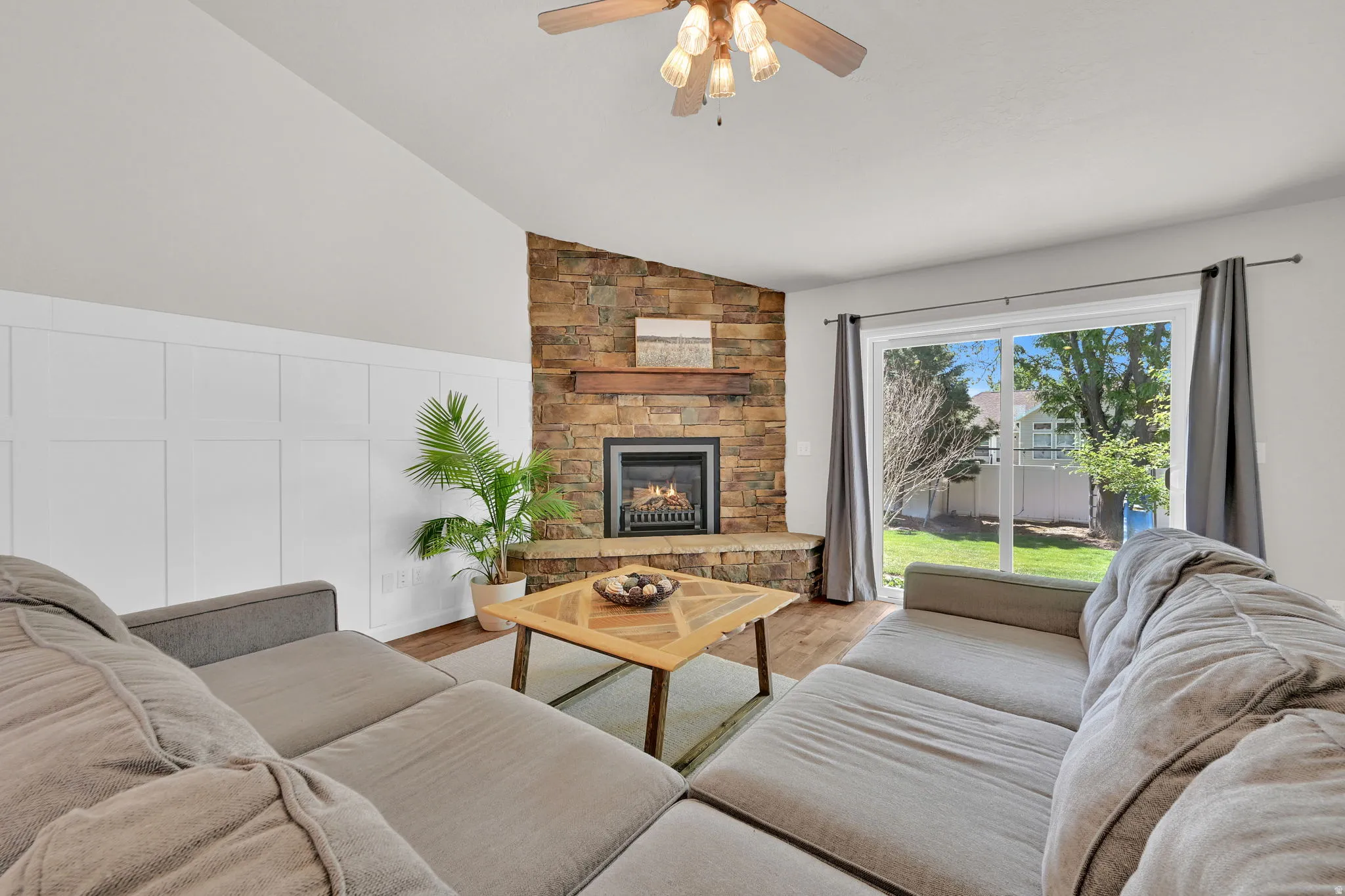 Living area featuring a stone-clad fireplace with a wood mantle, vaulted ceiling, and wood-finish flooring