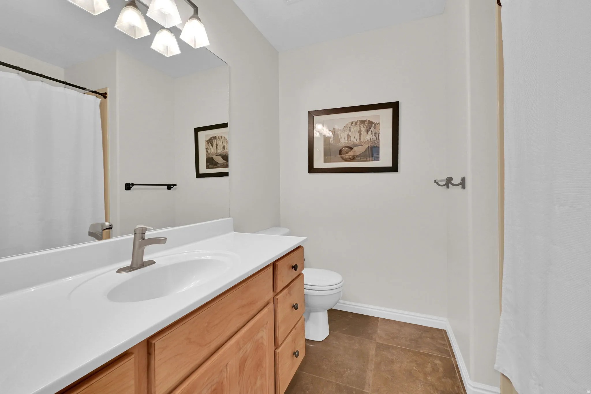 Bathroom featuring a light wood-finish vanity with a white countertop and integrated sink, brushed nickel faucet, large wall mirror, and brown floor tiles