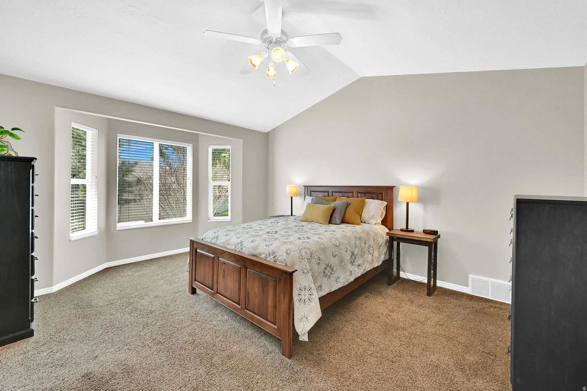 Bedroom featuring a vaulted ceiling with a ceiling fan, a bay window with multiple panes, and neutral-toned carpeting