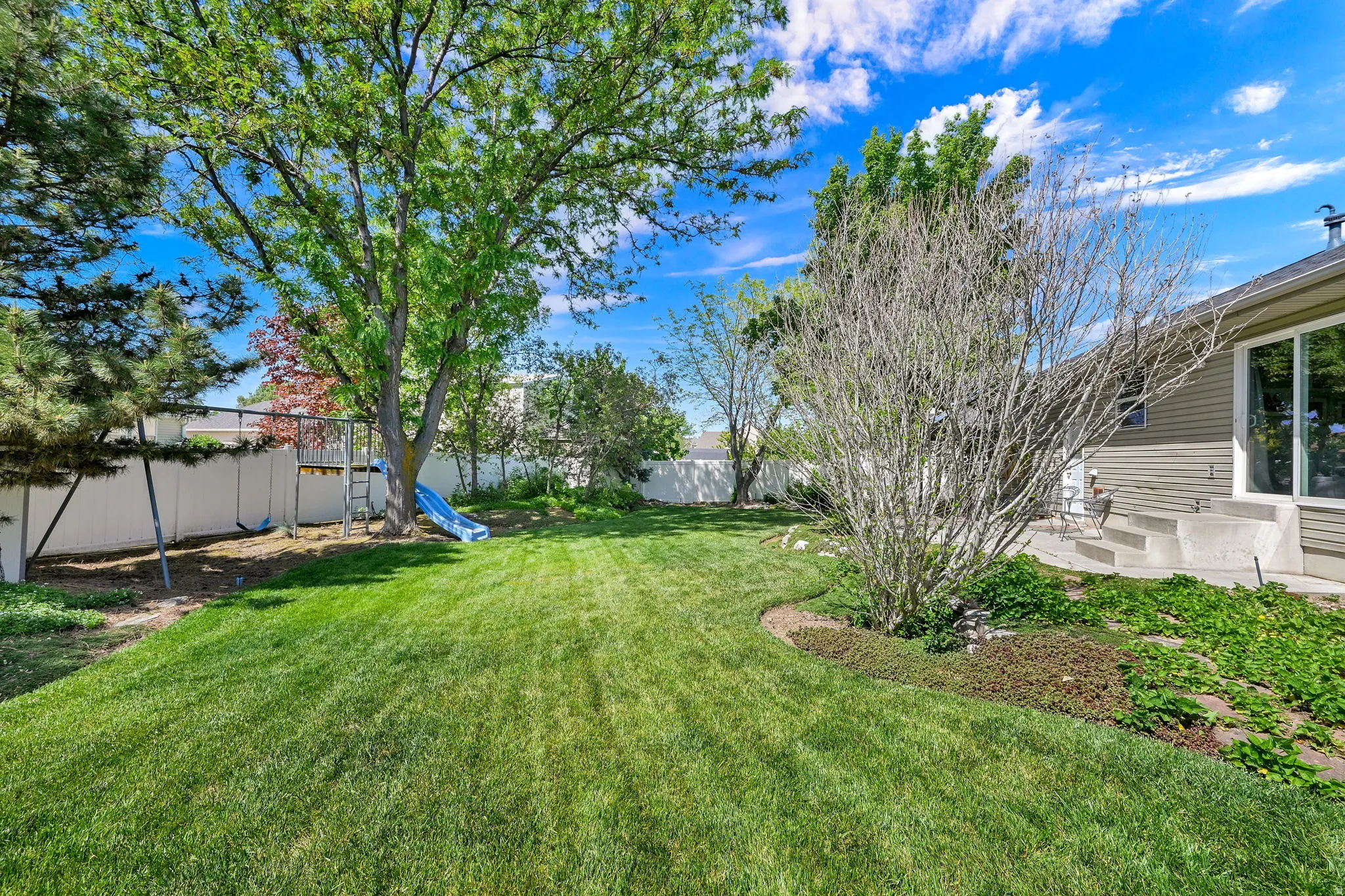 Expansive backyard featuring a lush lawn, mature trees, concrete patio, and a privacy fence
