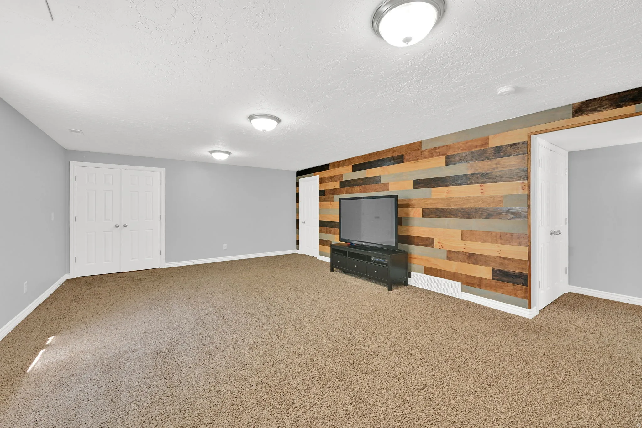 Spacious room featuring a multi-toned wood plank accent wall, neutral carpeting, and light gray painted walls