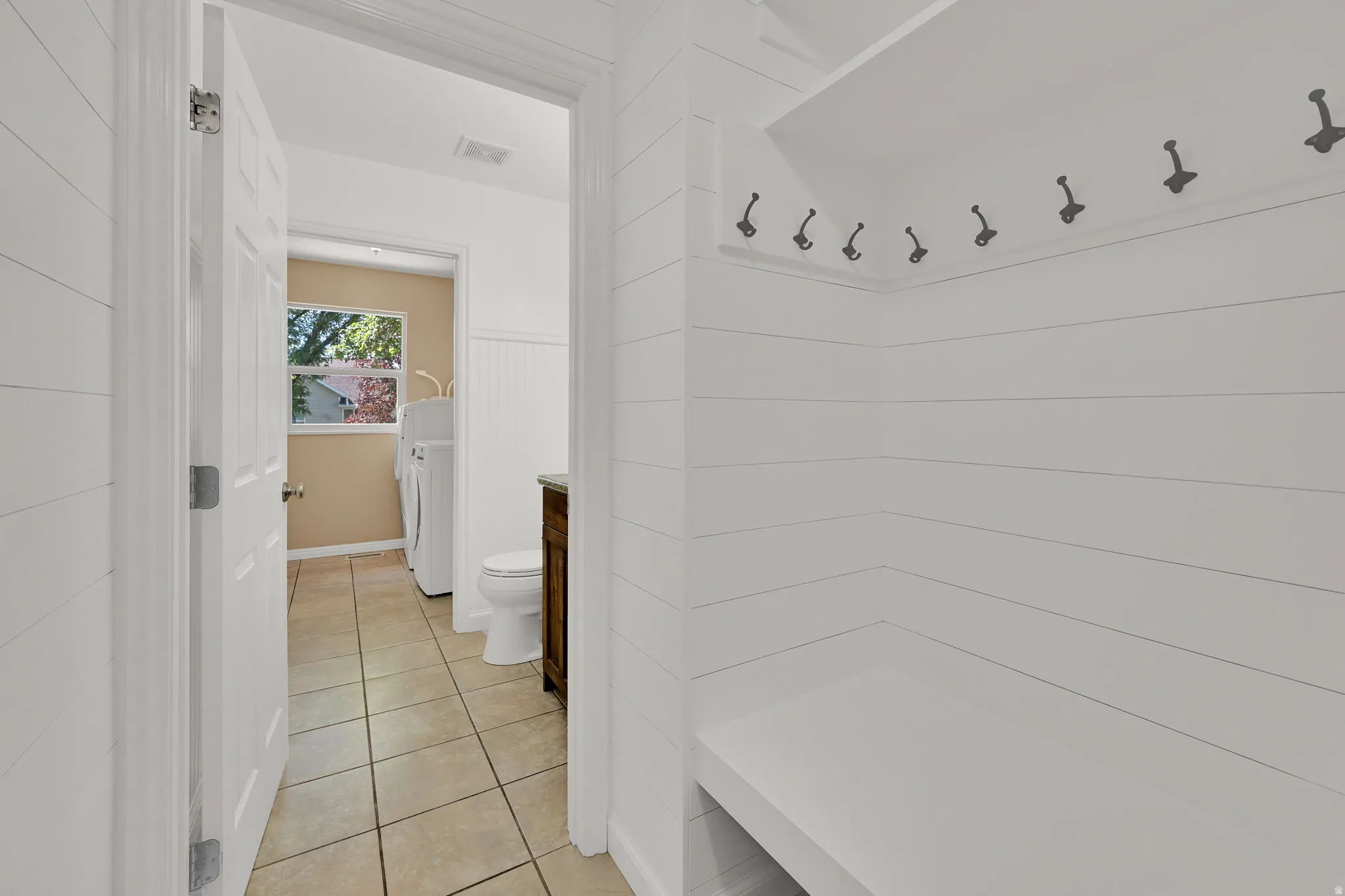 Mudroom area featuring white shiplap walls, a built-in bench, and coat hooks