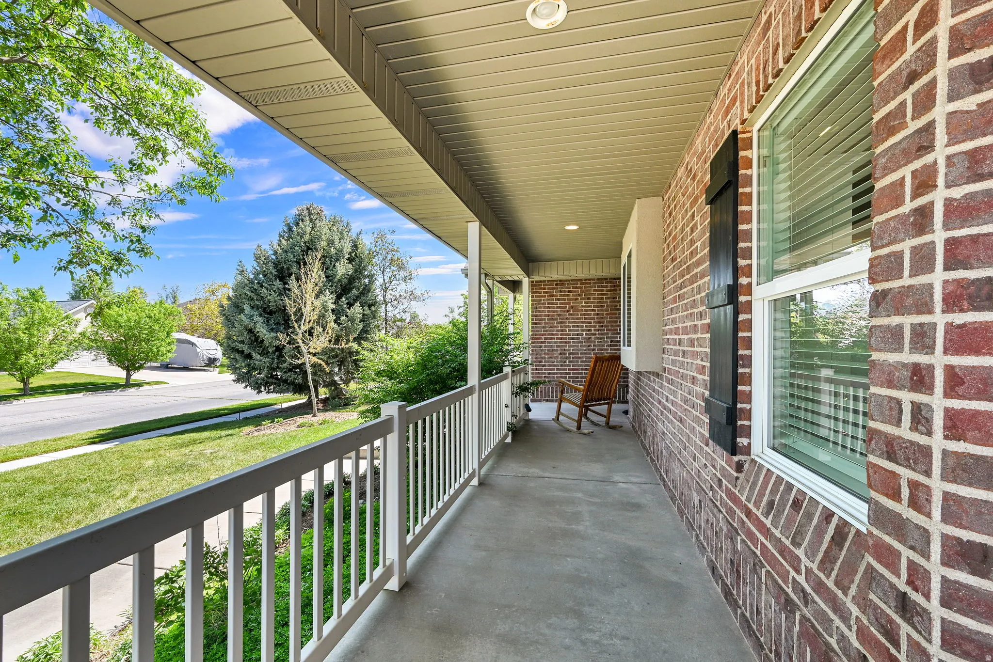 Covered front porch featuring a concrete surface, white railings, and a brick exterior