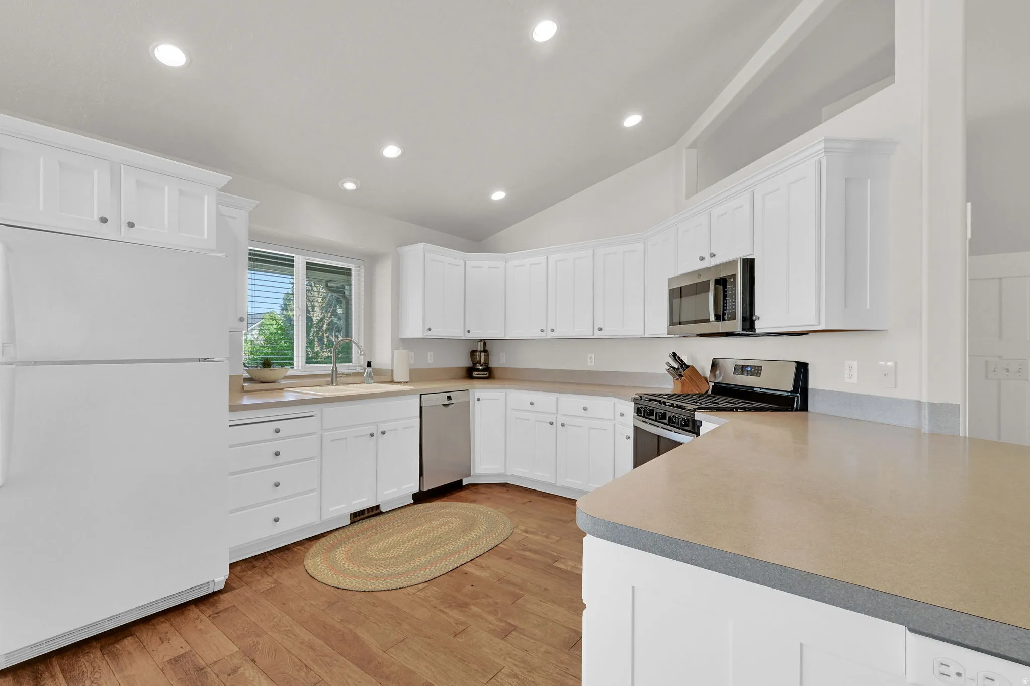 Spacious kitchen featuring extensive white cabinetry, durable wood-finish flooring, recessed lighting, stainless steel appliances, and a double basin sink beneath a window
