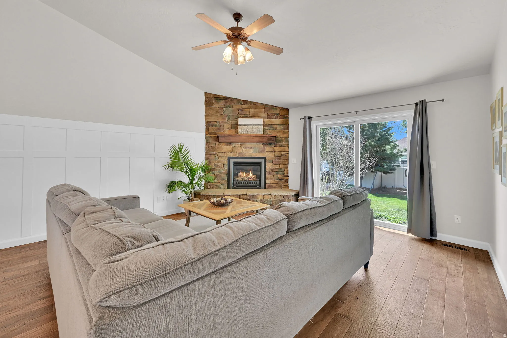 Living area featuring vaulted ceilings, wood-finish flooring, and a stone-clad fireplace with a wood mantel