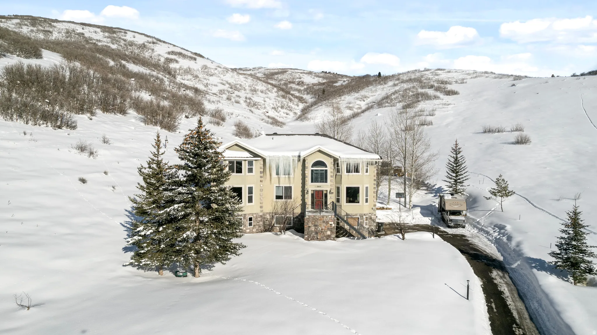 Contemporary multi-level residence featuring a neutral-toned exterior, stone accents, and a dark asphalt driveway