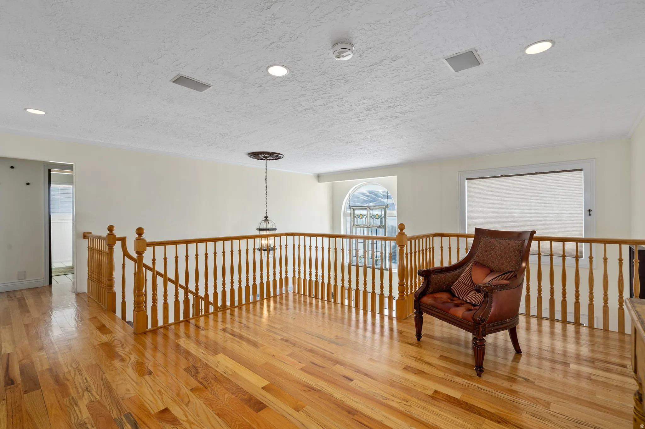 Hardwood flooring on an upper-level landing, featuring a wood spindle railing