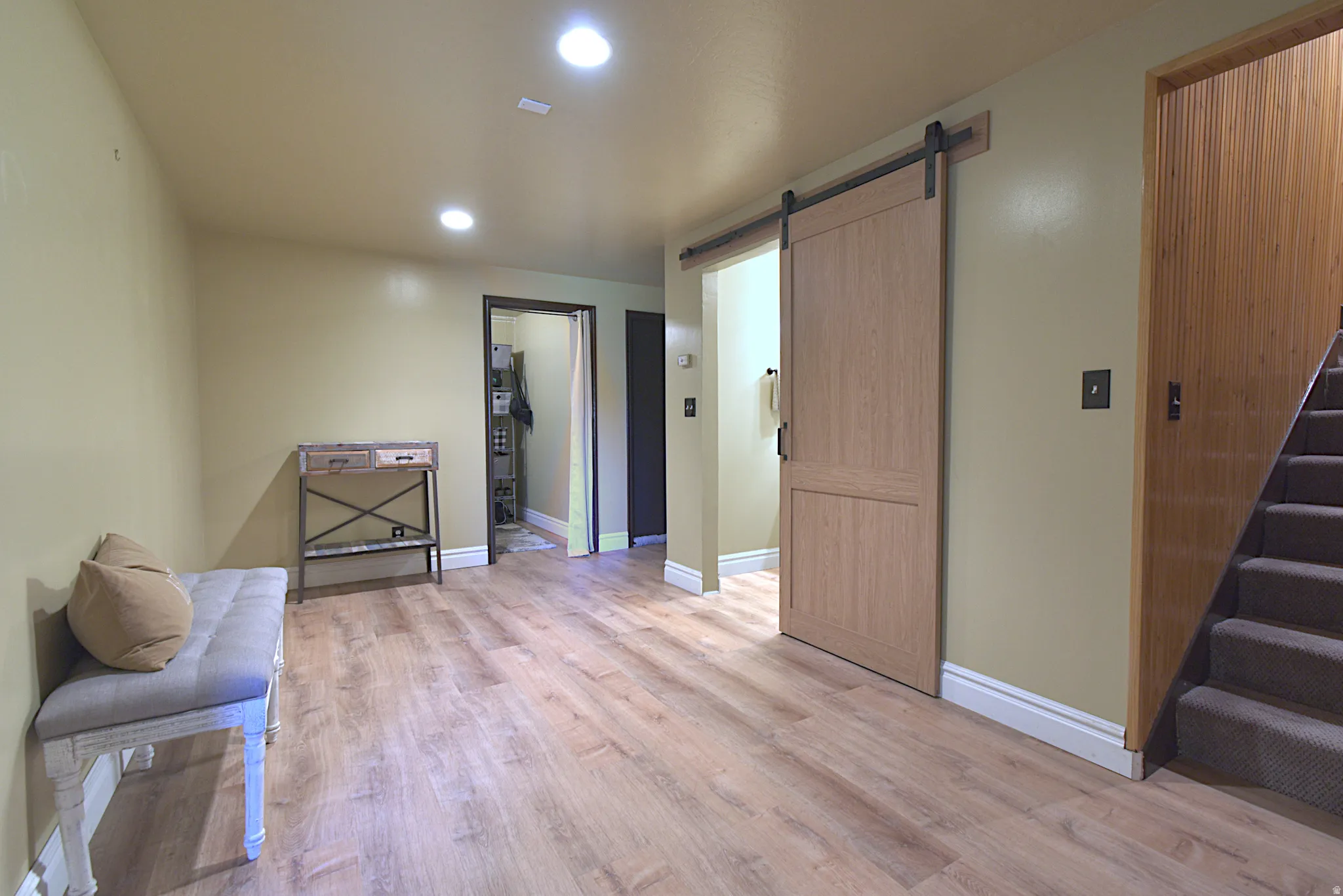 Wood-finish flooring throughout, featuring a modern barn door entry, recessed lighting, and a carpeted staircase with wood paneling