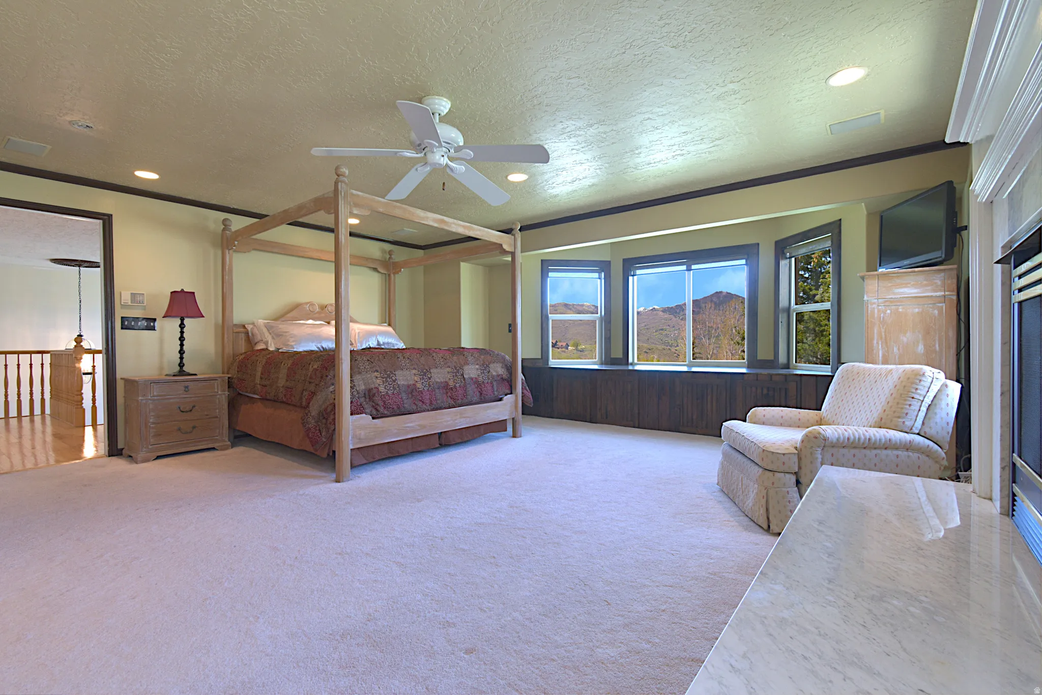 Spacious room featuring light-toned carpeting, a built-in window seat with storage, a white ceiling fan, recessed lighting, and a fireplace with a light-toned hearth