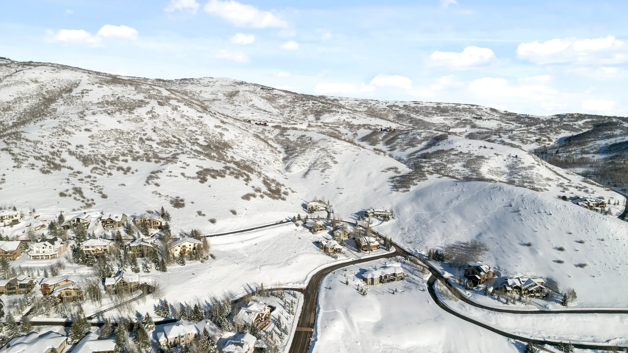 Snow-covered mountainous terrain featuring scattered residential properties and winding roadways