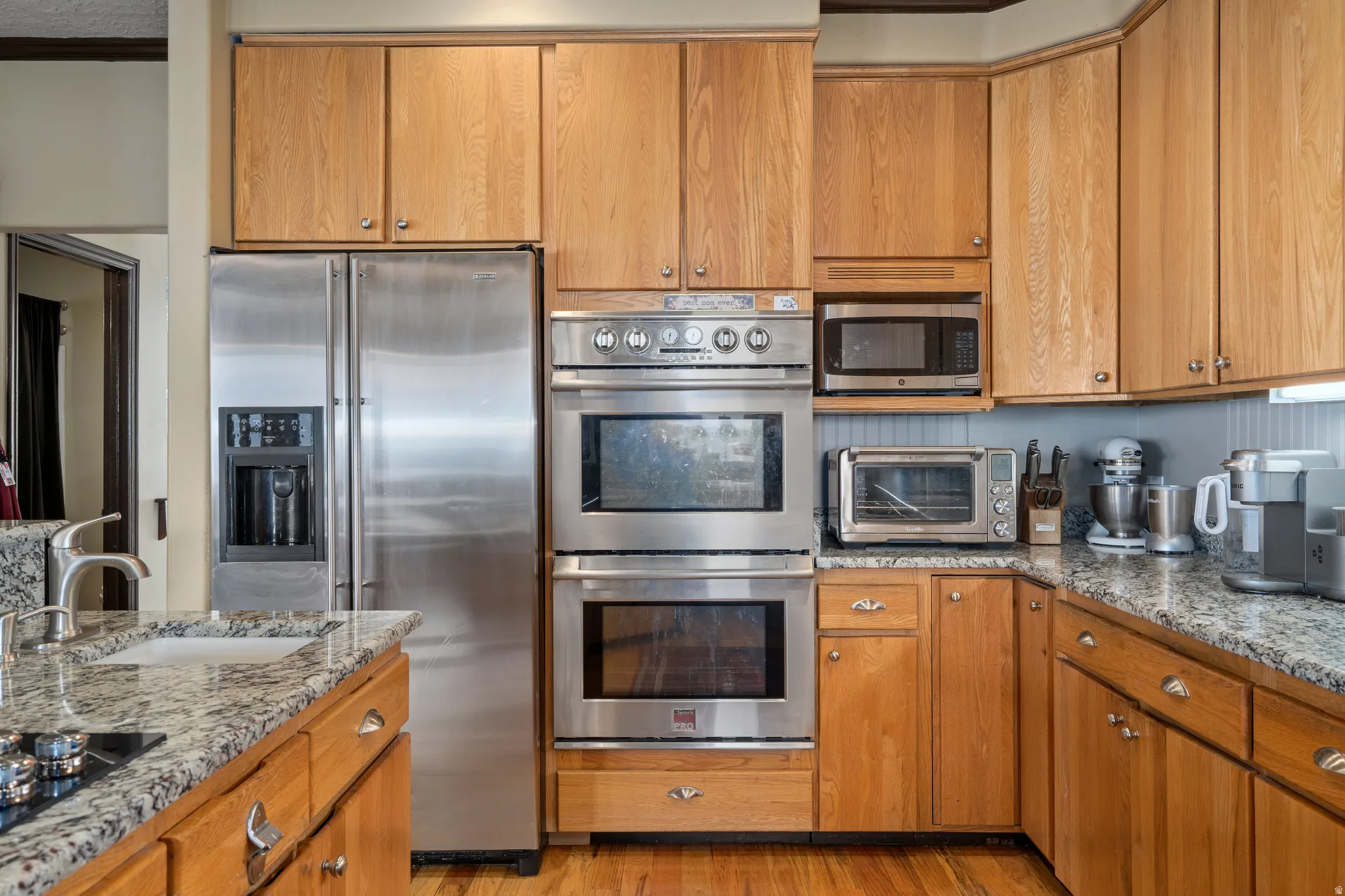 Kitchen featuring light wood cabinetry, stainless steel appliances, granite countertops, and wood-finish flooring