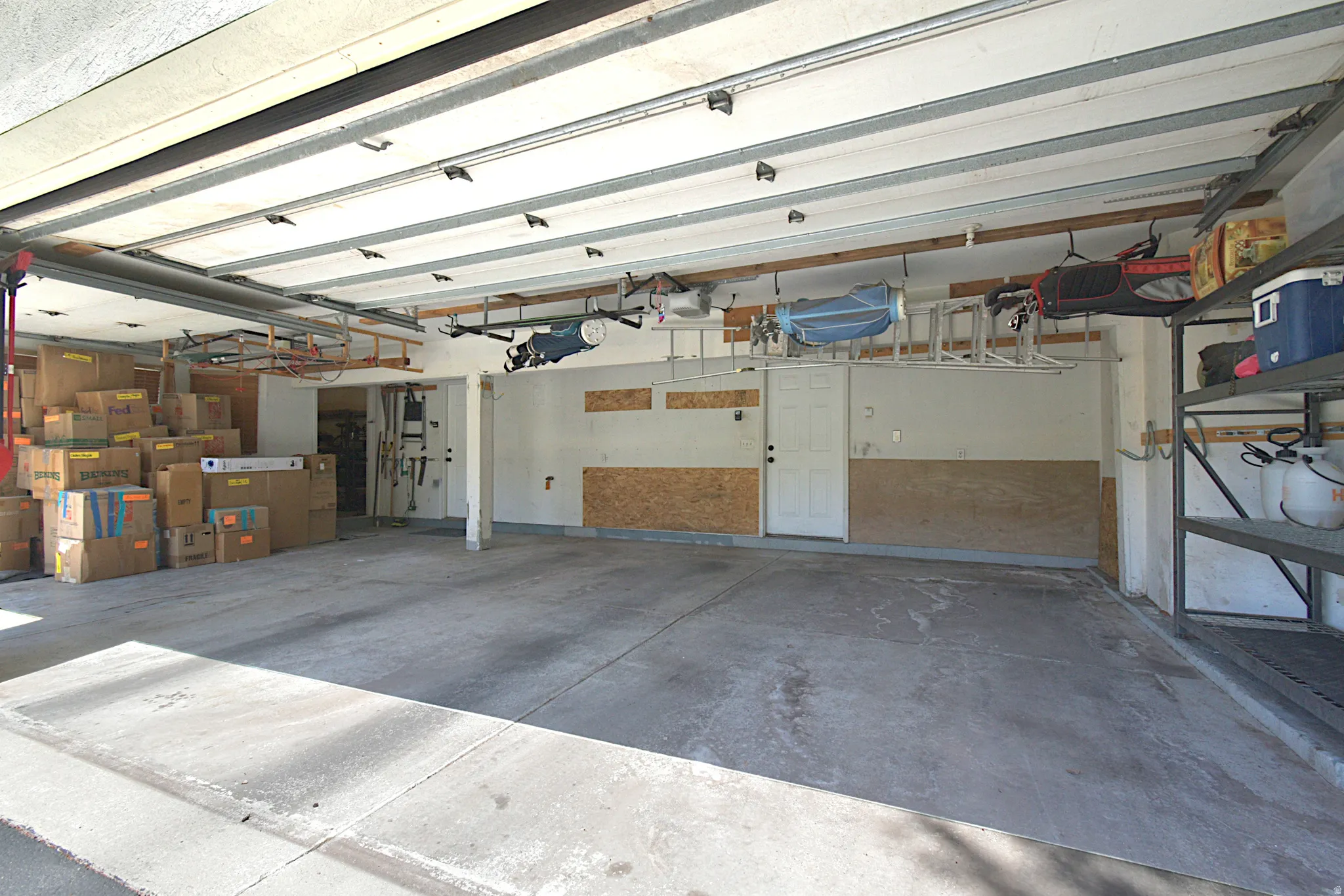 Spacious garage featuring a concrete floor, built-in shelving, overhead storage racks, a side entry door, and a partially finished wall