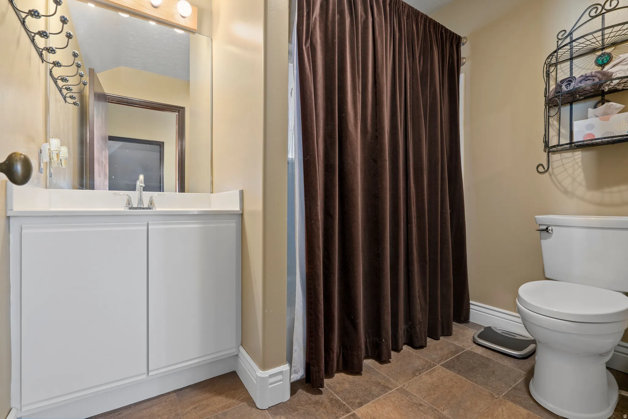 Bathroom featuring a white vanity with an integrated sink, a wall-mounted mirror, and a shower area with a brown curtain