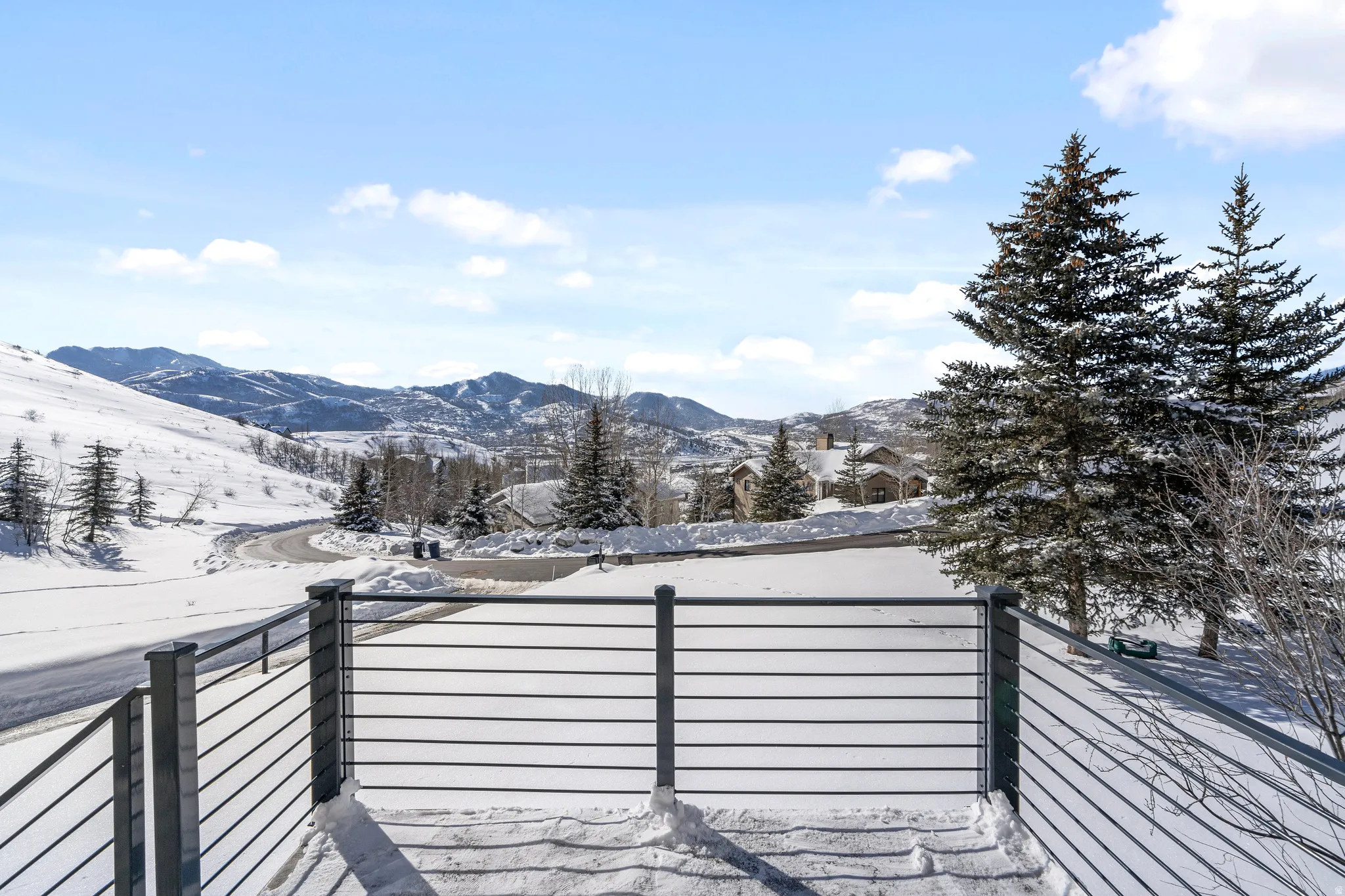 Outdoor balcony with horizontal metal railings, showcasing a sweeping mountain landscape with snow-covered terrain