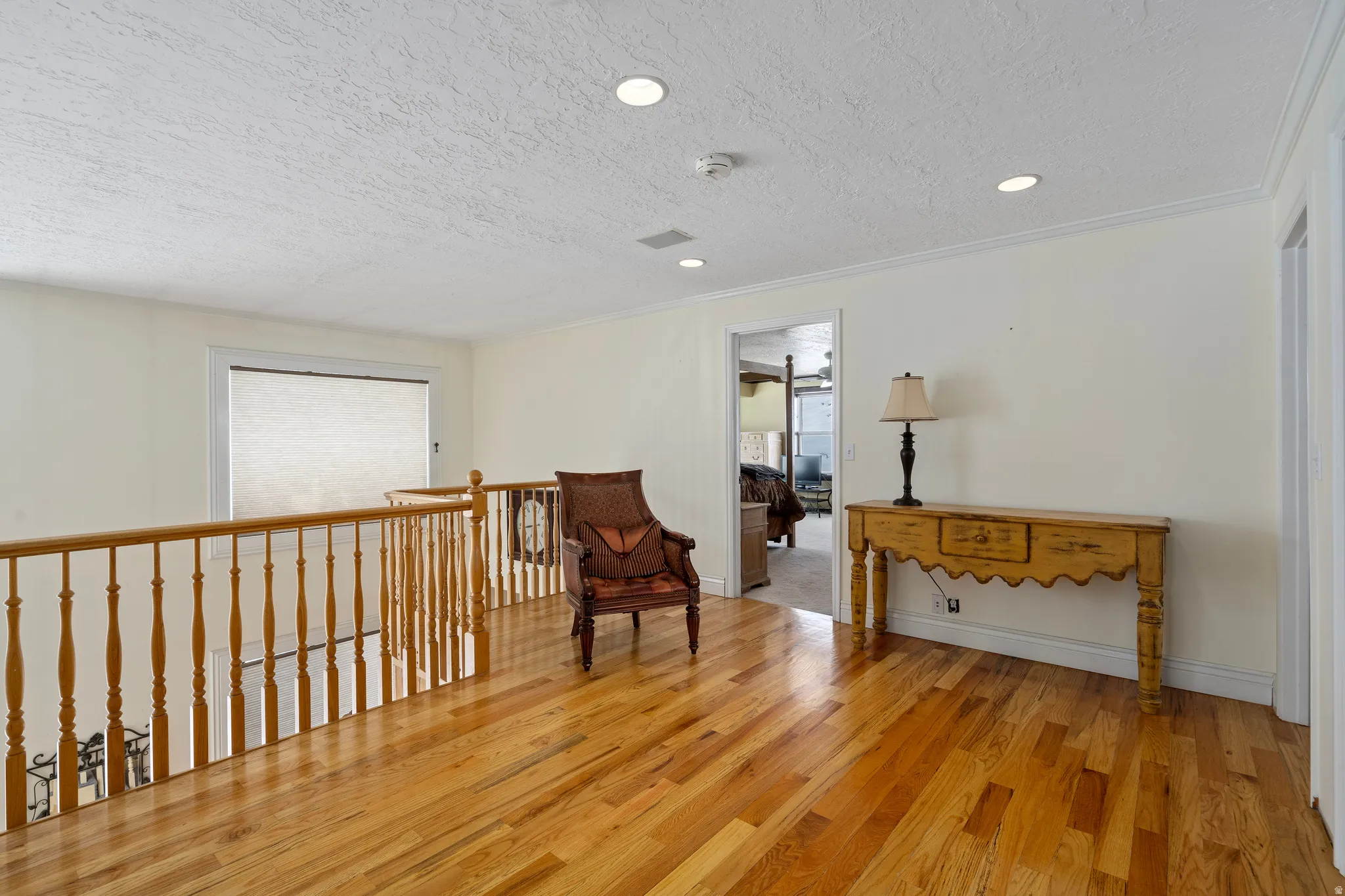 Open loft area featuring wood-finish flooring, light-toned walls, recessed lighting, and a wood banister