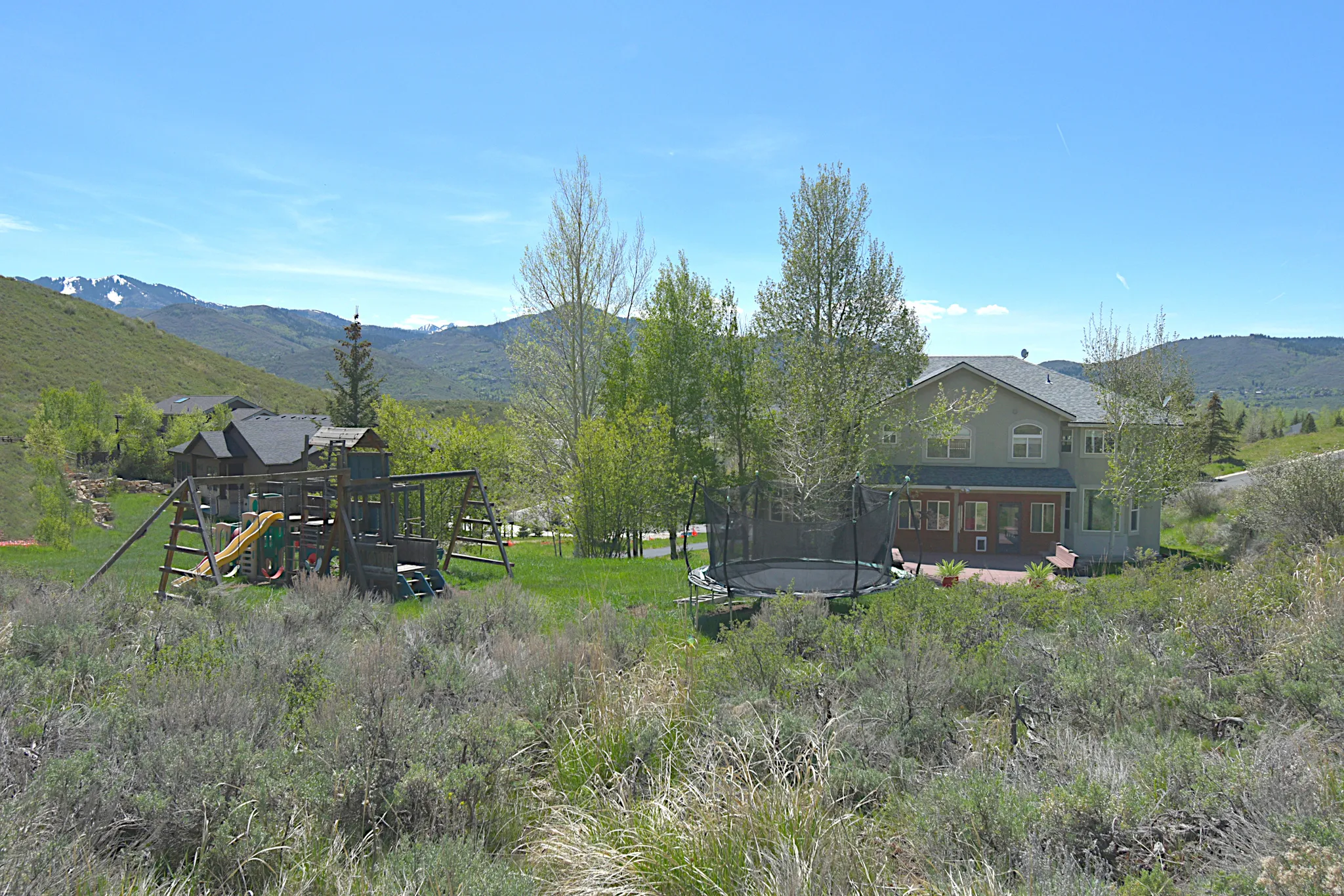 Spacious rear yard with a multi-level playset and mature trees