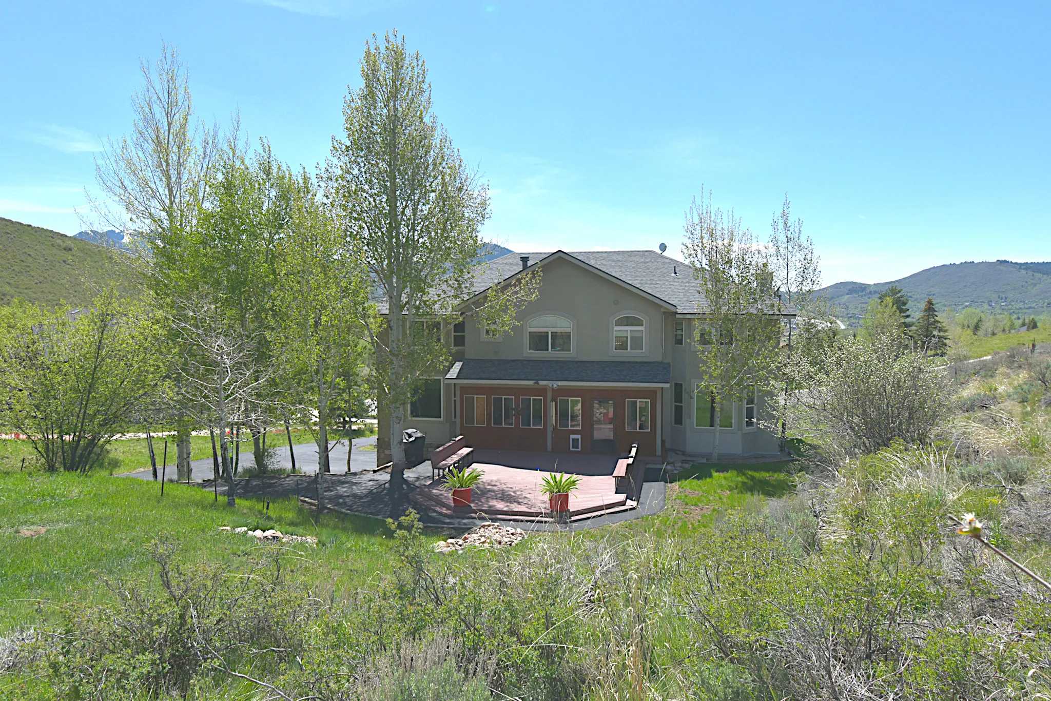 Spacious rear exterior featuring an expansive multi-level deck, mature trees, and a mountain backdrop