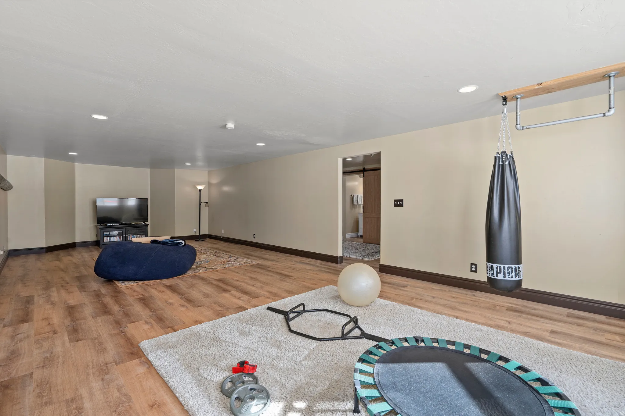 Spacious recreation room featuring wood-finish flooring, recessed lighting, and a barn door entry to an additional space