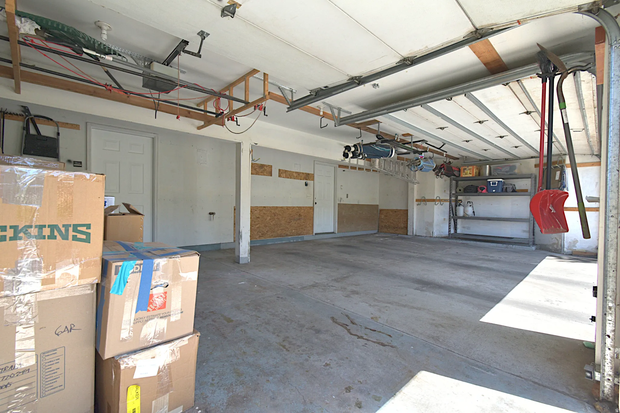 Two-car garage with concrete flooring, exposed ceiling beams, and overhead garage door mechanisms