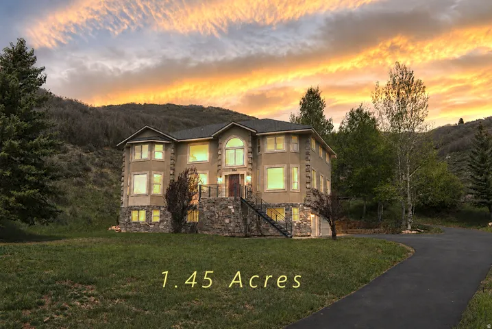 Stucco and stone exterior home featuring multiple large windows, a prominent arched window, a covered front entry with steps, and a paved driveway