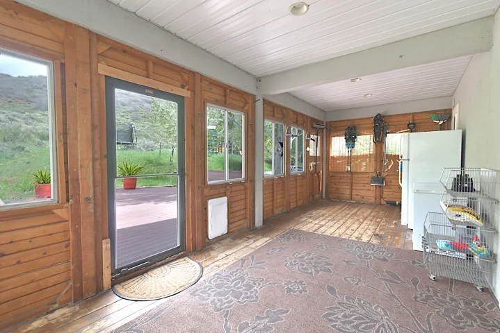 Covered porch featuring wood-panel walls, wood-finish flooring, and multiple window openings