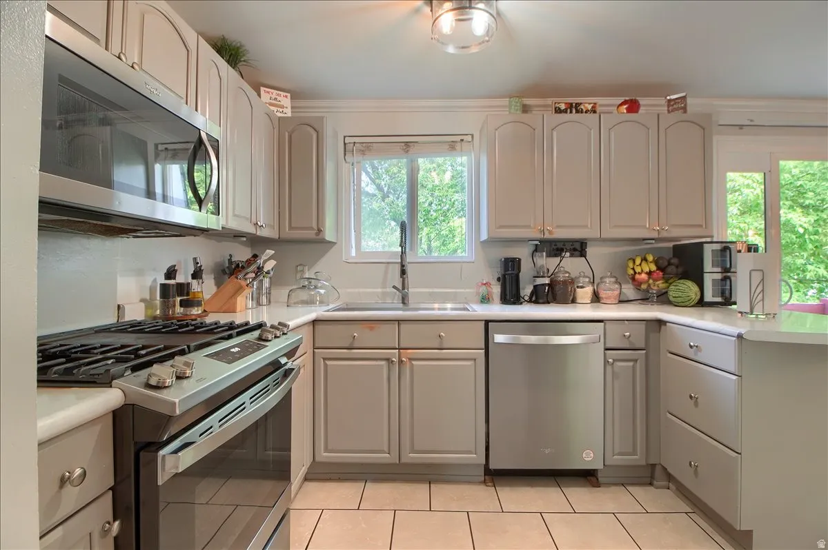 Kitchen featuring light-toned cabinetry, stainless steel appliances, a window above the sink, light countertops, and tile flooring