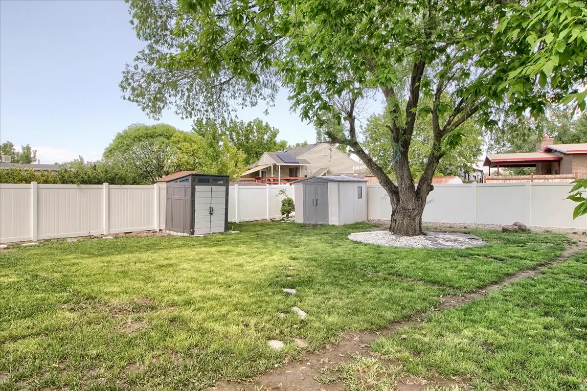 Expansive rear yard featuring mature tree, vinyl fencing, two storage sheds, and a manicured lawn