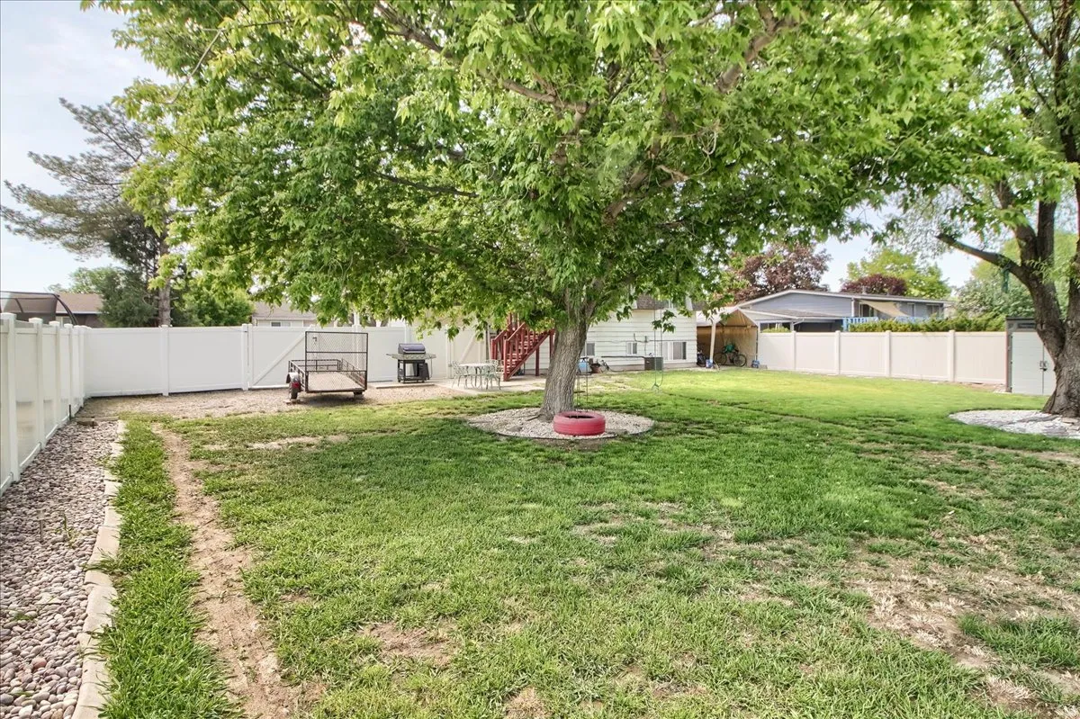 Spacious backyard with mature shade trees and a white privacy fence