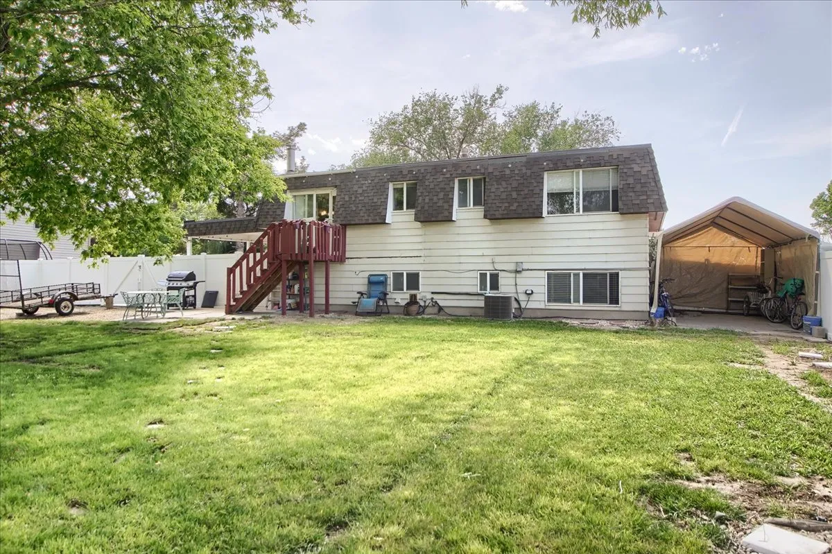 Spacious backyard featuring a manicured lawn, an upper-level deck with stairs, and a patio area