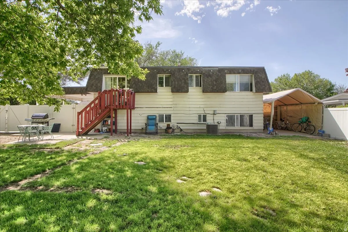 Spacious backyard with a vibrant green lawn, featuring a concrete patio area, privacy fencing, and an upper-level wood deck with stairs