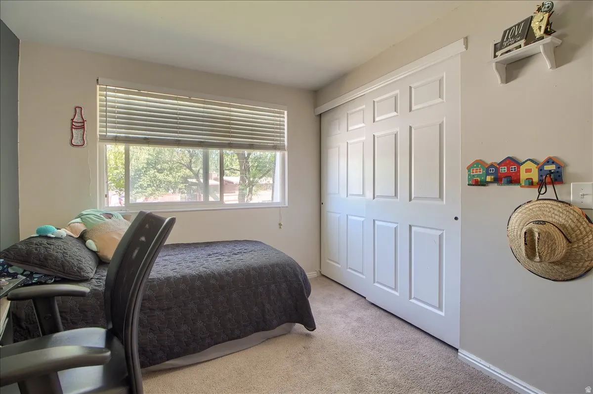 Bedroom featuring a carpeted floor, window with horizontal blinds, and a built-in closet with white paneled sliding doors