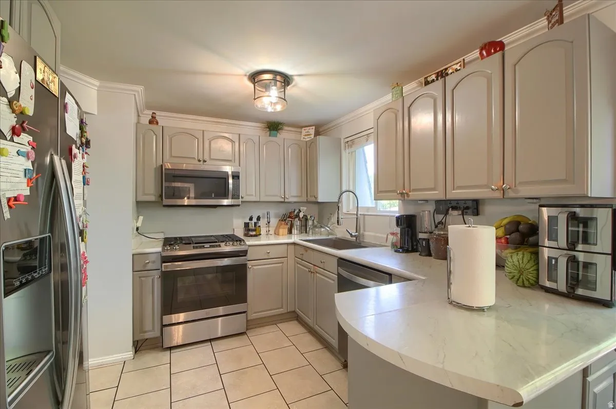 Well-appointed kitchen featuring light gray cabinetry with crown molding, stainless steel appliances, and a curved peninsula countertop