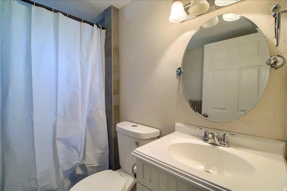 Bathroom featuring a white toilet, beadboard vanity with integrated sink, and an oval mirror