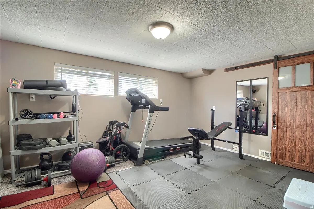 Dedicated room featuring two windows with blinds, a textured ceiling, neutral wall paint, and a wood-finish barn door with frosted glass panels